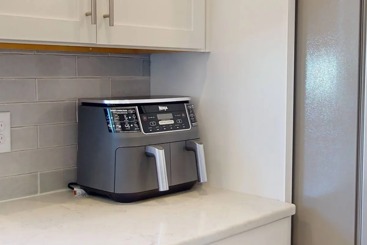 A contemporary kitchen corner showcasing an air fryer on the countertop, sleek cabinetry, and a stainless steel refrigerator. The setup is ready for quick, convenient meal prep, highlighting thoughtful extras for guests.