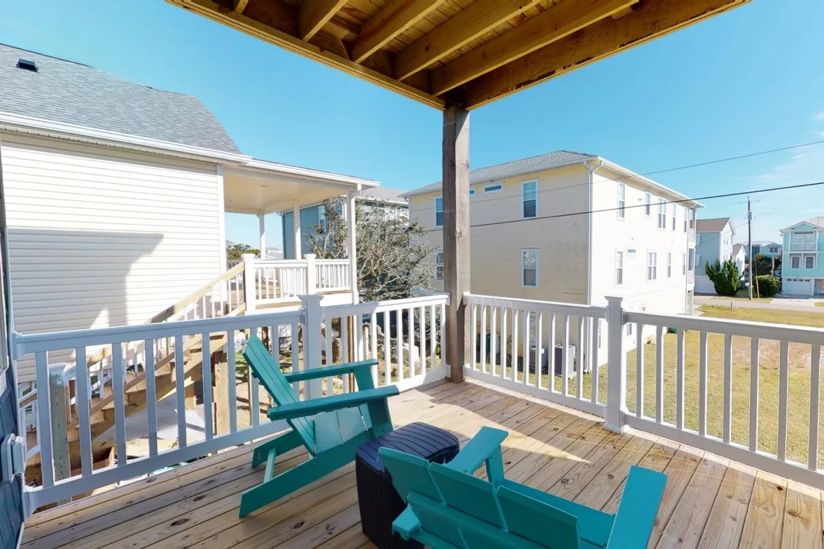 This photo captures a tranquil wooden deck with adirondack chairs and a white railing, overlooking what appears to be a sunlit coastal view. It's an inviting spot for sipping coffee, cocktails, or simply soaking in the ambiance.