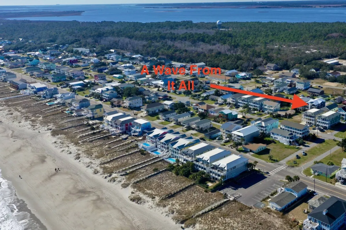 A serene exterior view of beachfront homes with the ocean and sandy shoreline in the frame. The boardwalk stretches toward the beach, inviting visitors to stroll along the coast. Gentle sunlight creates a welcoming mood, and the entire scene radiates the appeal of seaside living and neighborhood gatherings.