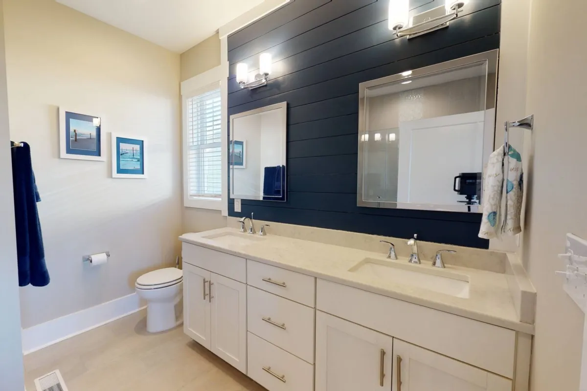 A spa-like bathroom with double vanity, elegant mirrors, blue accent wall, and tasteful framed art. The space is bright, calm, and designed for soothing morning and evening routines.