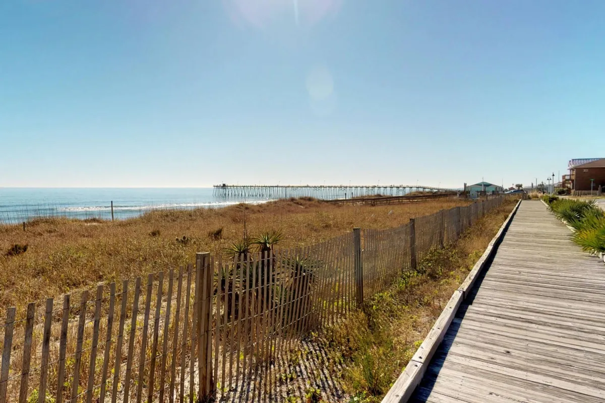 A wide view of the beach, pier, boardwalk, and ocean with dune grasses gently swaying in the breeze. The tranquil setting encourages exploration, relaxation, and romantic moments such as stargazing or sunset walks.