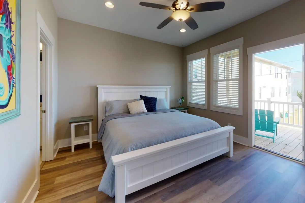 A serene bedroom featuring a comfortable bed, artwork above the headboard, a nightstand with lamp, and a window letting in soft natural light. The room exudes calm and is designed for relaxation, making it ideal for restful nights or enjoying a quiet morning coffee.