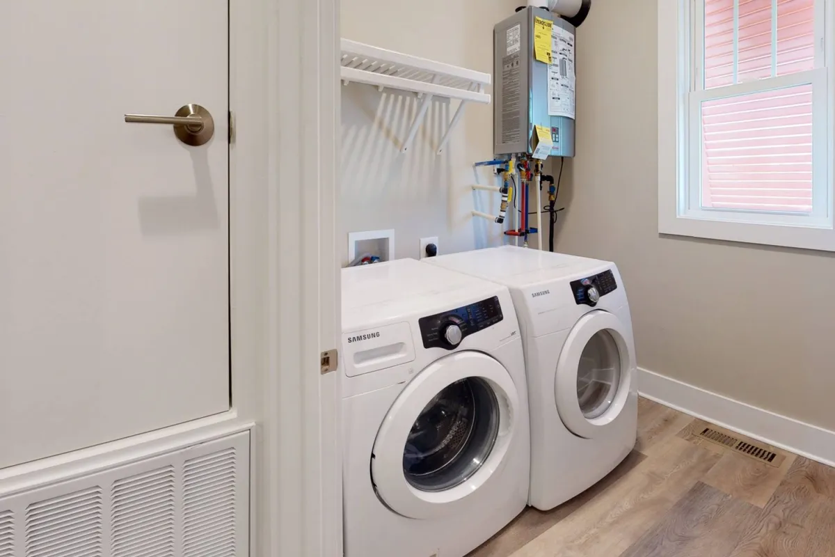 A bright, functional laundry area featuring a modern washer and dryer, open shelves for storage, and a window that lets in natural light. The space is organized and ready for handling beach towels or everyday laundry needs.
