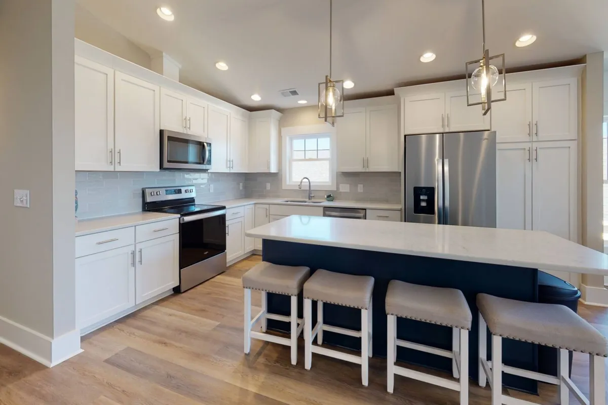 A modern kitchen is depicted with a central island and seating, stainless steel appliances, and crisp white cabinetry. The space is functional and inviting, perfect for cooking or enjoying a casual breakfast together. The kitchen’s design hints at quality, contemporary amenities.