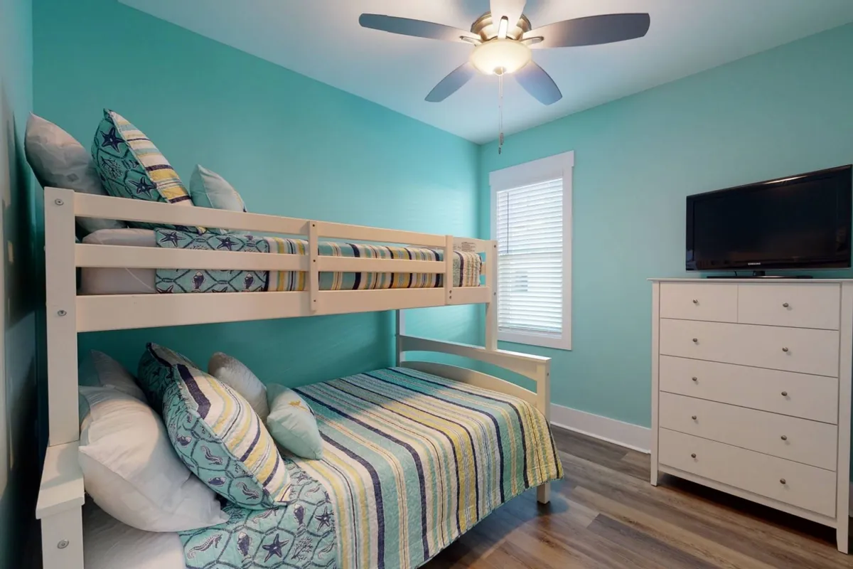 A playful bunk room with colorful striped bedding, a sturdy bunk bed, wall-mounted TV, and dresser. The space is inviting for kids and perfect for sleepovers, featuring cheerful decor and a relaxed atmosphere.